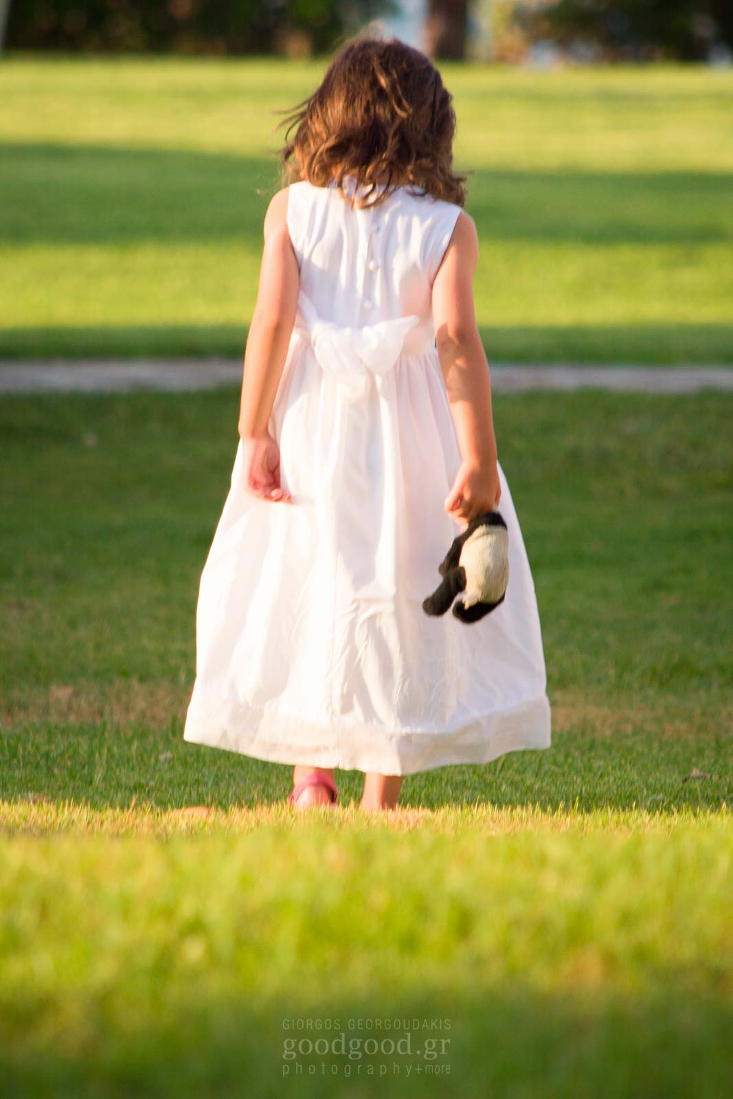 Baptism photo of a little girl standing on the grass holding a doll