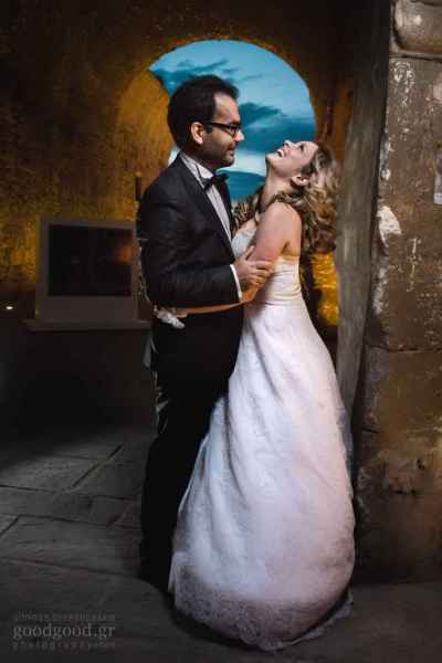 Φωτογραφία ενός γαμπρού και μίας νύφης να στέκονται και να γελάνε στα ενετικά νεώρια του Ηρακλείου Κρήτης