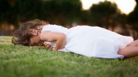 Photo of a girl in a white dress rolling on the grass and laughing