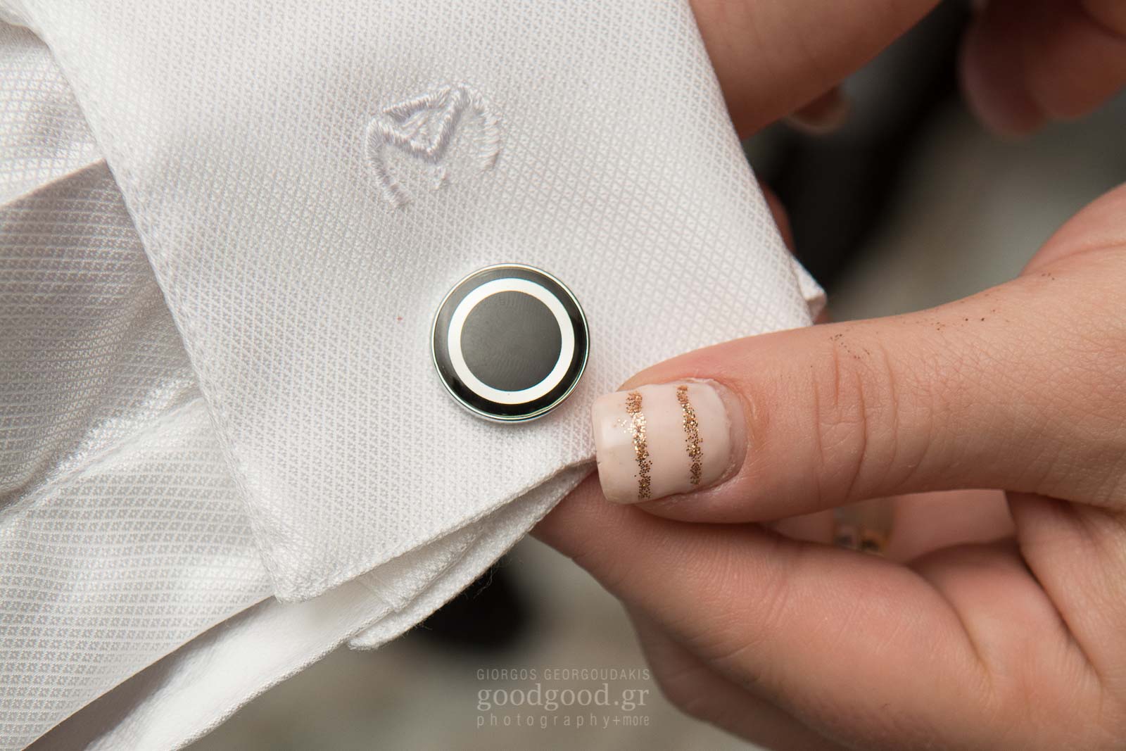 Close up photo of a woomans hand holding the groom's cufflink